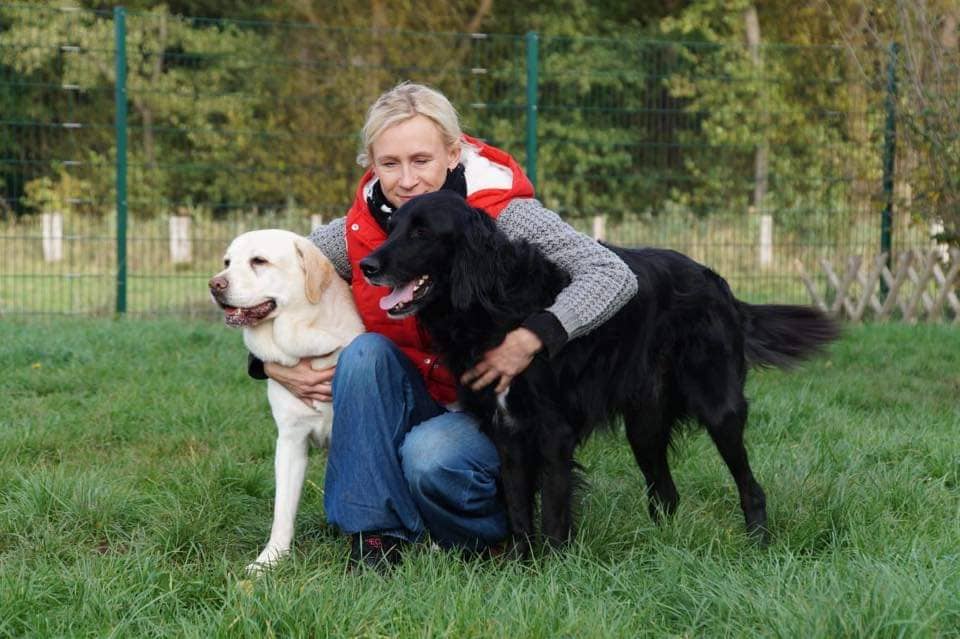 Betreuerin umarmt zwei Hunde auf der Wiese des Auehofs