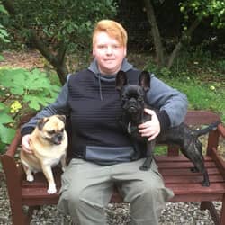 Sarah Könemann auf einer Gartenbank, links ein heller Mops-Mischling, rechts eine schwarze Französische Bulldogge